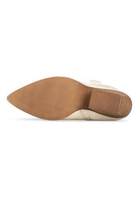 Zapato color crema con punta estrecha y puntiaguda, un tacón bajo en bloque y una suela de goma texturizada. Cuenta con una correa lateral como detalle.