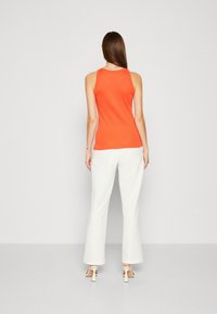 Top arancione senza maniche abbinato a pantaloni ampi bianchi, che mostrano un design attillato con una texture liscia e uno stile minimalista.