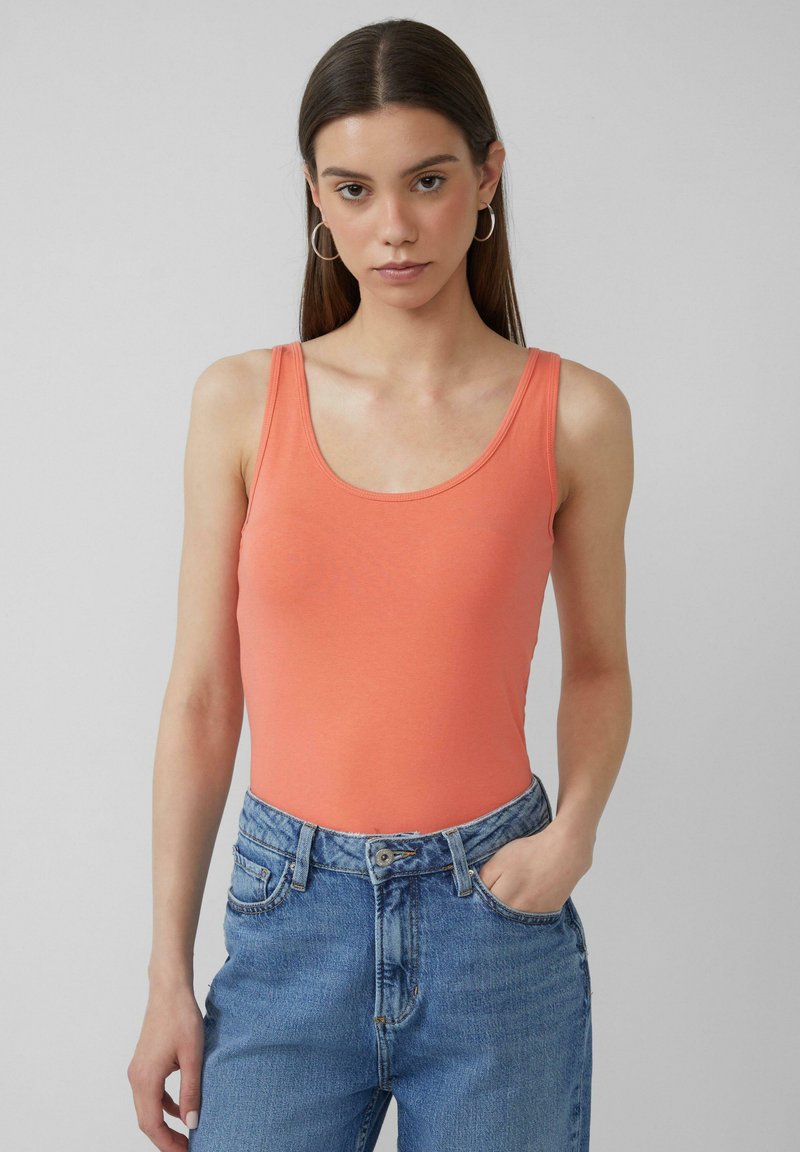 Perzikkleurig tanktop in een getailleerd ontwerp, gemaakt van ribbelmateriaal met brede schouderbanden. Gepaard met high-waisted blauwe spijkerbroek.