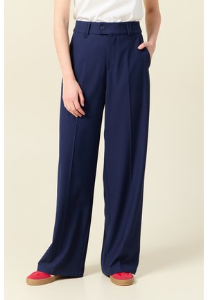Navy wijde pantalons van gladde stoffen, met een hoge taille, voorplooien en twee zijzakken. Gecombineerd met rode schoenen.