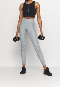 Czarny sportowy crop top, szare legginsy o heatherowej teksturze oraz czarne buty sportowe. Sztangi trzymane w obu rękach, pozycja stojąca.