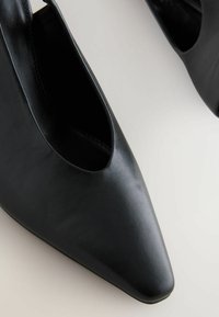Musta nahkakengät terävällä varvalla, joissa on leikattu muotoilu. Tasainen pinta ja minimalistinen tyyli. Ei näkyvää metalliosaa tai koristelua.