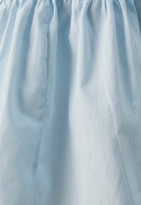 Gonna in cotone azzurro chiaro con vita arricciata. La superficie appare liscia con leggere pieghe e drappeggi per volume.