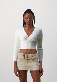 Bílý žebrovaný dlouhý rukáv crop top s hlubokým výstřihem do V a béžová kordová mini sukně s širokým páskem a dvěma předními kapsami.