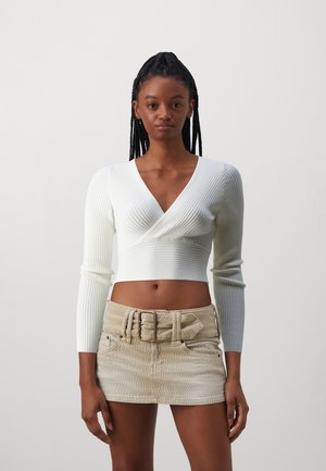 Weißes, geripptes Langarm-Crop-Top mit tiefem V-Ausschnitt und beiger Cordmini-Rock mit breitem Gürtel und zwei vorderen Taschen.