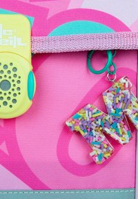 Gelbes Plastikmikrofon mit türkisfarbenen Akzenten, pinkfarbenem strukturiertem Hintergrund und einem klaren Buchstaben-Anhänger, der mit bunten Streuseln gefüllt ist.