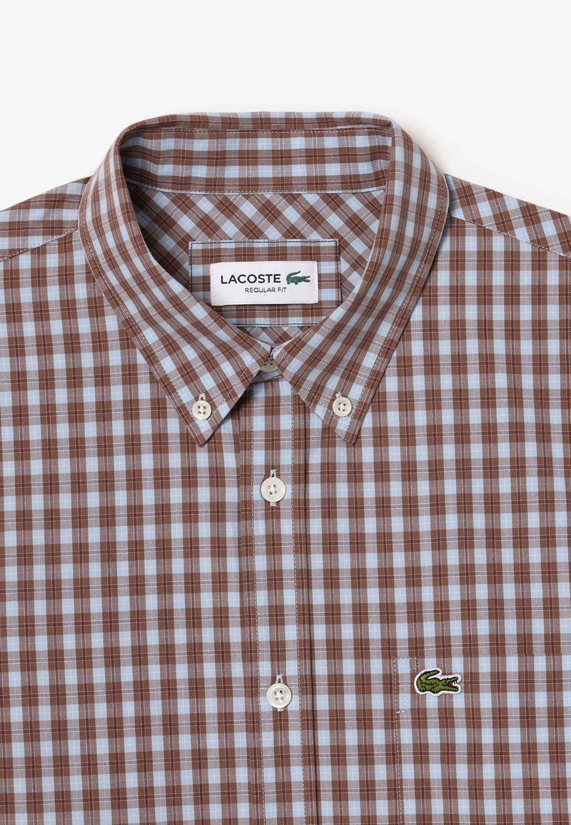 Chemise à carreaux marron et bleu clair à boutons. Matière en coton avec une coupe régulière, dotée d'un col, de boutons blancs et d'un logo de crocodile vert.