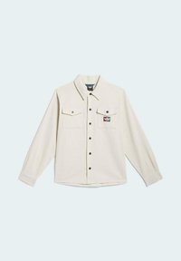 Camisa beige claro de manga larga, con dos bolsillos en el pecho, cierre de botones al frente y una pequeña etiqueta de marca en el bolsillo izquierdo. Botones negros.