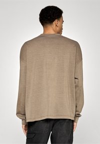 Garas piedurkņu taupe krāsas džemperis ar brīvu piegriezumu, apaļu kakla izgriezumu un aprocēm uz piedurknēm. Izgatavots no mīksta auduma, ar vienkāršu dizainu.