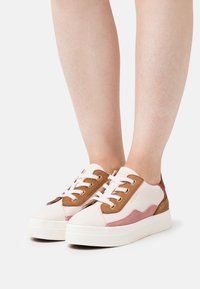 Zapatillas con parte superior de cuero blanco, acentos de ante marrón y paneles laterales rosas. Presentan una suela de plataforma blanca y cordones blancos.