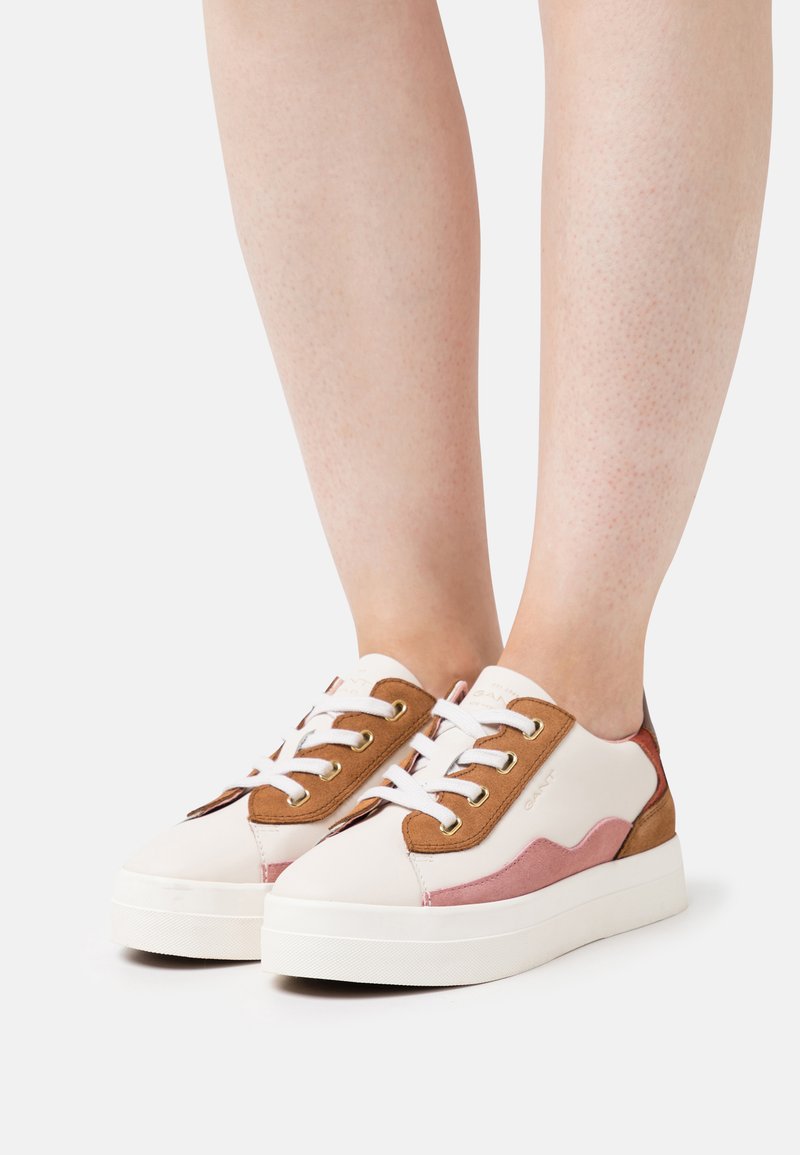 Zapatillas con parte superior de cuero blanco, acentos de ante marrón y paneles laterales rosas. Presentan una suela de plataforma blanca y cordones blancos.