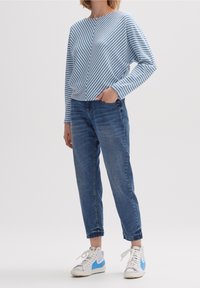 Niebiesko-biały sweter w paski z wzorem w kształcie litery V, połączony z jasnoniebieskimi dżinsami i białymi trampkami z niebieskimi akcentami.