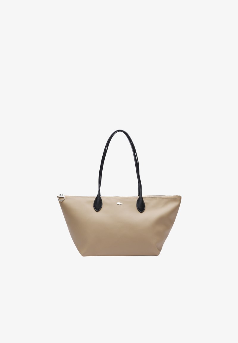 Torba typu tote w beżowym materiale syntetycznym z czarnymi skórzanymi akcentami. Posiada dwa długie uchwyty oraz logo na środku. W kształcie trójkąta.