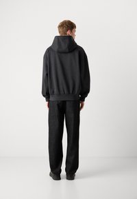 Felpa nera con un ampio cappuccio regolabile, polsini a costine e vita elasticizzata, abbinata a pantaloni neri a vestibilità larga. Tessura liscia.