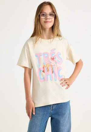Cremefarvet bomuld t-shirt med teksten "TRÈS CHIC" i pink og blå, samt et grafik af en isvaffel. Kortærmet og afslappet pasform.