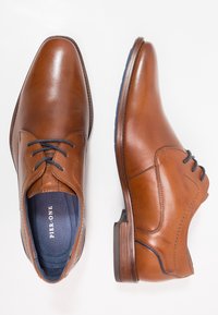 Braune Lederschuhe mit glattem Finish, spitzer Zehenpartie und hellblauen Akzenten an der Sohle. Mit traditionellen Schnürsenkeln und gesteppten Details versehen.