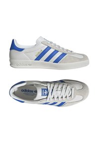 Classiche sneakers Adidas Gazelle in bianco con accenti blu e grigi, caratterizzate da tre strisce blu e una suola texturizzata.