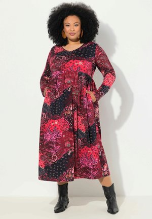 Robe à manches longues en rose et bleu marine avec des motifs floraux et géométriques, dotée de poches latérales et d'une jupe fluide. Associée à des bottines noires.