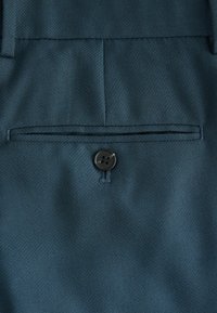 Tmavě modrozelená látka se hladkým povrchem, s jednobuttonovým zapínáním a detailem zadní kapsy.