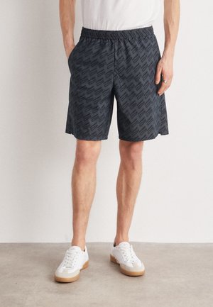 Sorte mønstrede shorts med elastisk linning, sidelommer og løs pasform, kombineret med hvide sneakers med gummisåler.