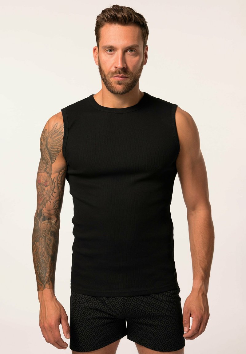 Top in maglia a costine nera senza maniche con una vestibilità aderente. Il modello indossa pantaloni corti scuri con fantasia. Il tono della pelle è medio con tatuaggi visibili.