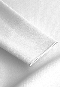 Weißer texturierter Stoff, leicht aufgerollt, zeigt ein feines Gewebemuster mit glatter Oberfläche und sauberen Kanten. Reflektiert sanft natürliches Licht.