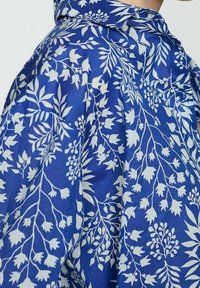 Blue fabric with white floral pattern; incorporates leaves and small flowers; smooth texture; features a collar and loose fit design.