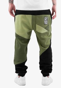Pantaloni verzi și negri, cu croială lejeră, dotati cu o buzunar aplicat, design colorat și manșete elastice, confecționați dintr-un material moale din amestec de bumbac.