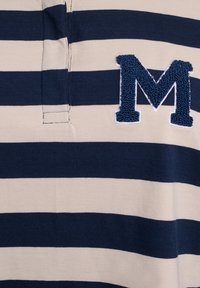 Puuvillane polo särk, millel on tumesinised ja kreemjad horisontaalsed triibud, rinnal on sinine broderitud "M" logo ning nööpide rida.