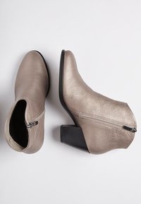 Stivali ankle metallici color taupe con superficie texturizzata, cerniera laterale e tacco spesso nero. Design elegante con punta affusolata.