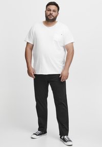Hvid bomulds T-shirt med brystlomme, parret med sorte bukser og sorte sneakers. Casual pasform og ensfarvede nuancer med minimale detaljer.