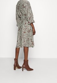 Blommig midiklänning i ljusgrön med röda och bruna mönster. Har lösa ärmar och ett bälte vid midjan. Matchas med bruna ankelskoot.