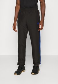 Pantalones deportivos negros con franjas laterales azules, cinturilla elástica y piernas ajustadas. Combinados con zapatillas deportivas negras.