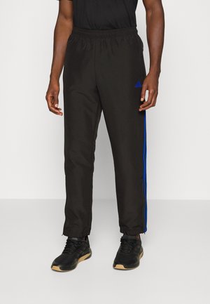 Pantalones deportivos negros con franjas laterales azules, cinturilla elástica y piernas ajustadas. Combinados con zapatillas deportivas negras.