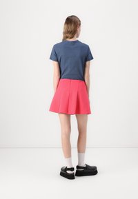 T-shirt en coton marine, jupe plissée rose et chaussures à plateforme noires avec boucles. La tenue comprend des manches courtes et une silhouette longueur genou.