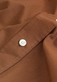Gros plan sur un tissu marron avec un bouton blanc visible et une boutonnière cousue sur un vêtement plié.