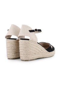 Sandalias de cuña de esparto negras con una correa texturizada de color crema, con detalle de hebilla y tacón envuelto en yute. Diseño de parte trasera abierta.