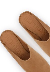 Chaussures à enfiler en daim beige avec une semelle intérieure en cuir lisse, présentant un logo embossé et un design minimaliste avec un bout arrondi.