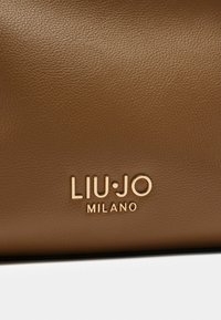 Pruuni tekstuurne nahast kott, millel on kuldne logo, kus on äänkse "LIU·JO MILANO". Lihtne disain puhaste joonte ja modernsete aktsentidega.