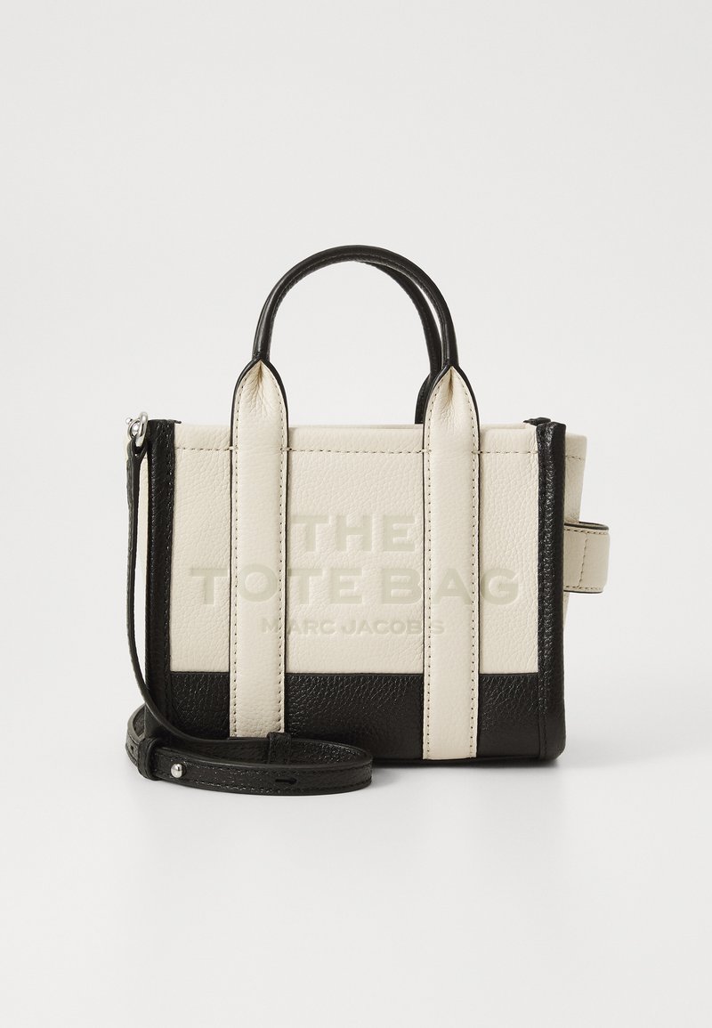 Mini tote bag made from textured cream and black leather, featuring dual handles, a detachable shoulder strap, and embossed logo details.