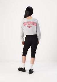 Grå sweatshirt med rød tekst "THE UPSIDE TOKYO 1999," sammen med svarte cropped bukser og robuste svarte sko, båret med hvite sokker.