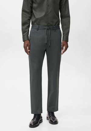 Pantalones de un gris oscuro, a medida, con una cinturilla elástica, textura suave y corte recto, combinados con zapatos negros y una camisa oscura.