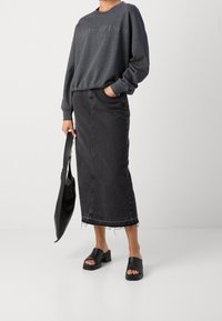 Grijze katoenen sweatshirt met reliëflogo, zwarte denim midi-rok met rafelige zoom, zwarte platform sandalen en een zwarte tote bag.