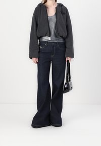 Sudadera negra de gran tamaño con cremallera, top metálico plateado, jeans de mezclilla oscura de pierna ancha, sosteniendo un bolso negro. Atuendo sencillo y casual.