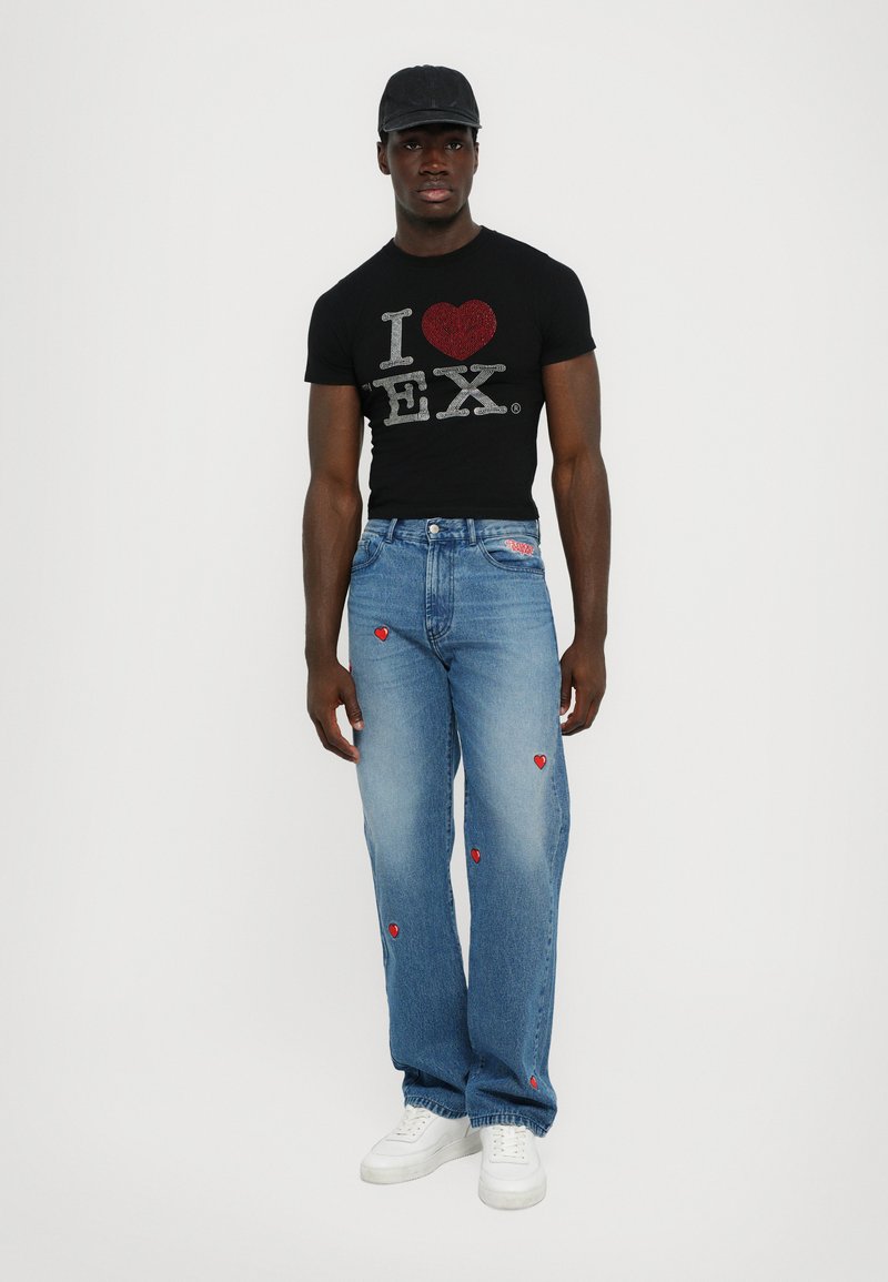 Tricou negru, mulat, cu grafica "I ♥ EX" și inimioare roșii; blugi deschiși, largi, cu broderie de inimă roșie, asortați cu teniși albi.