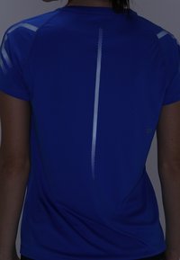 Krátký rukáv sportovní tričko v jasně modré barvě s reflexními diagonálními pruhy na ramenou a svislým pruhem na zádech.