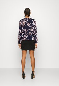 Camisa floral de mangas longas com padrão em azul-marinho e rosa, combinada com uma saia preta justa e sandálias de salto bloco pretas. Textura de tecido suave.