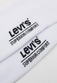 Fehér pamut zoknik fekete hímzett "Levi's" logóval és "Felsőfokú Kényelem" felirattal, sima felülettel és klasszikus sportos dizájnnal.