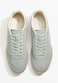 Hellgrüne Sneakers aus Textil und Wildleder. Sie verfügen über normale Schnürsenkel, eine abgerundete Spitze sowie einen kontrastierenden, cremefarbenen Kragen und eine Innensohle.