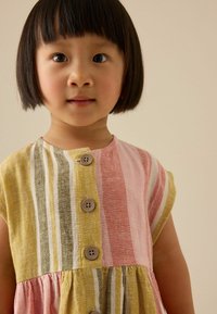 Robe rayée colorée à manches courtes, ornée de boutons, dans des teintes de rose, jaune, vert et d'une texture en lin blanc.